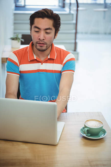 Uomo che utilizza computer portatile con tazza di caffè sul tavolo in caffetteria — Foto stock