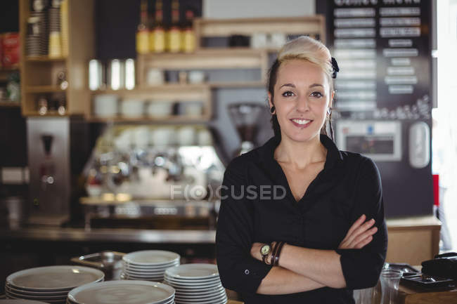 Retrato de garçonete de pé com os braços cruzados no café — Fotografia de Stock