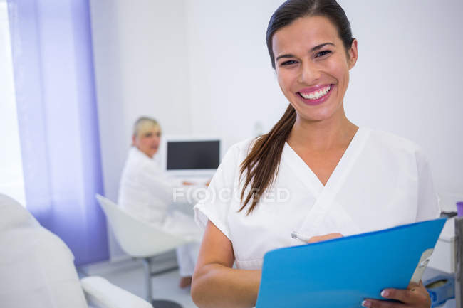 Retrato del dentista sonriente escribiendo informe médico en la clínica - foto de stock