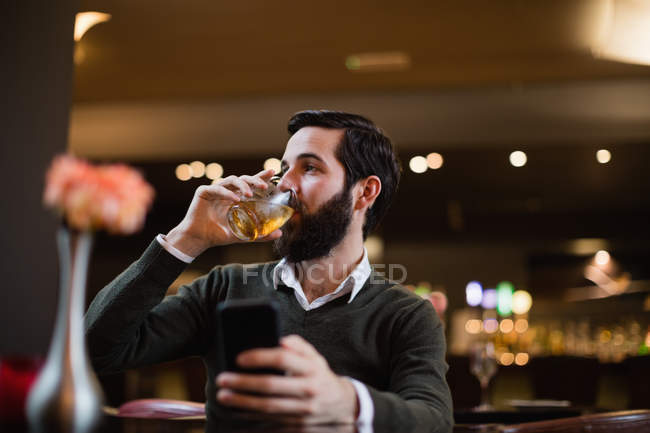 Homem segurando celular e tomando uma bebida no bar — Fotografia de Stock