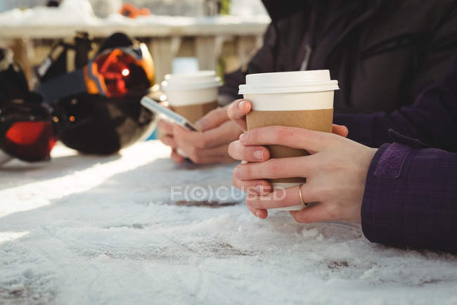 Sección media de la pareja con taza de café utilizando el teléfono móvil - foto de stock