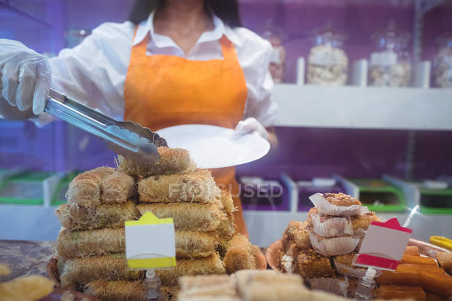 Female shopkeeper serving turkish pastries in plate at counter in shop — Stock Photo