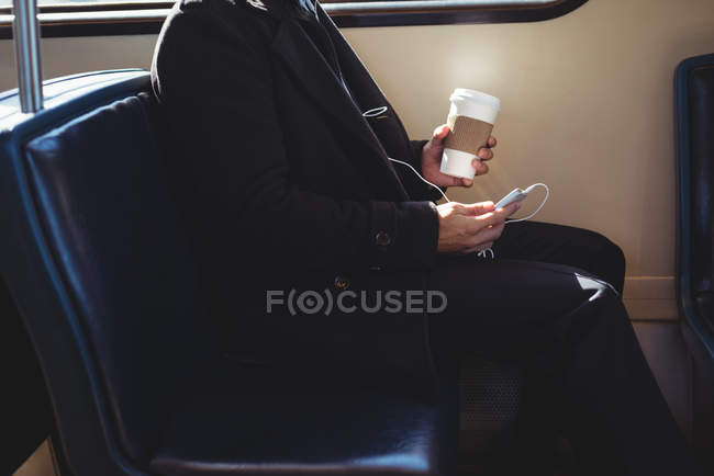 Середня секція бізнесмена, що тримає одноразову чашку кави та використовує мобільний телефон у потязі — стокове фото