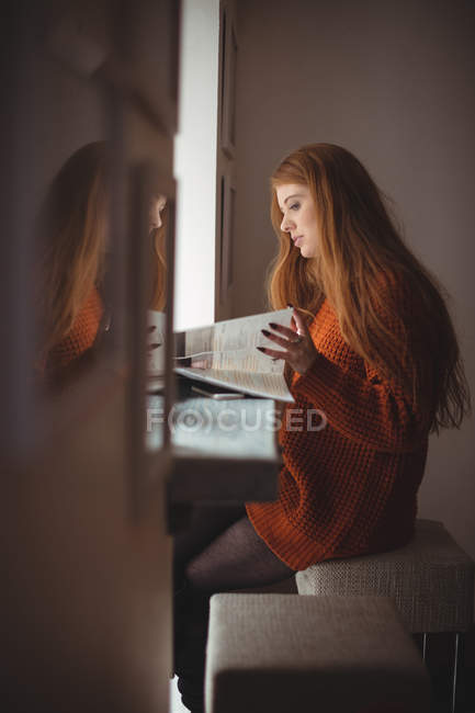 Junge Frau liest Buch am Fenster im Restaurant — Stockfoto
