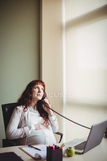 Schwangere Geschäftsfrau berührt Bauch beim Telefonieren im Büro — Stockfoto