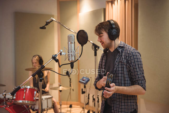 Чоловік співає з мікрофоном, граючи тамбур в музичній студії — стокове фото