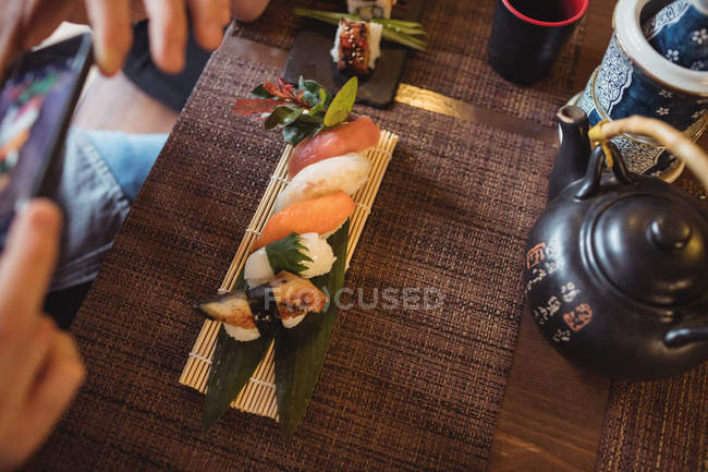 Hombre tomando fotos de sushi en el restaurante - foto de stock