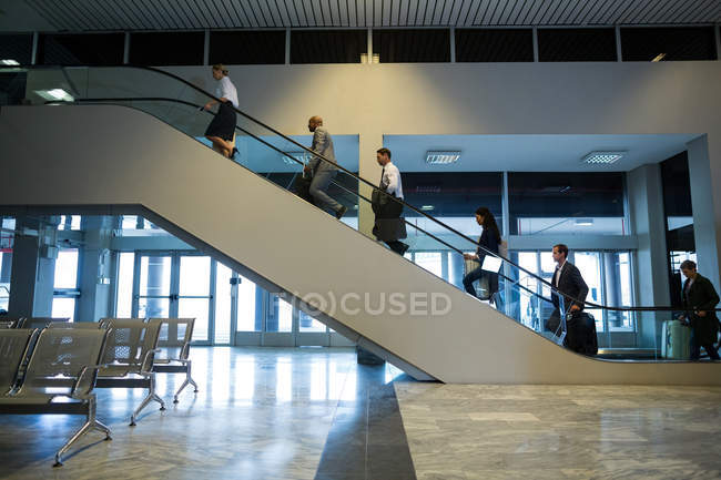 Gente de negocios en escaleras mecánicas en aeropuerto - foto de stock
