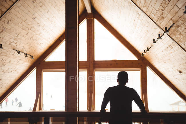 Чоловік стоїть всередині шале, насолоджуючись видом на гірськолижний курорт — стокове фото
