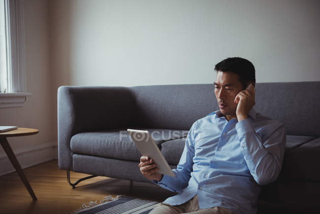 Чоловік розмовляє на мобільному телефоні, використовуючи цифровий планшет вдома — стокове фото