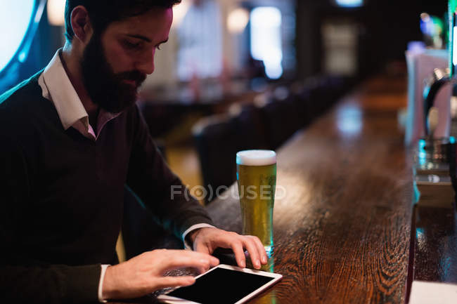 Businessman using digital tablet with glass of beer on counter in bar — Stock Photo