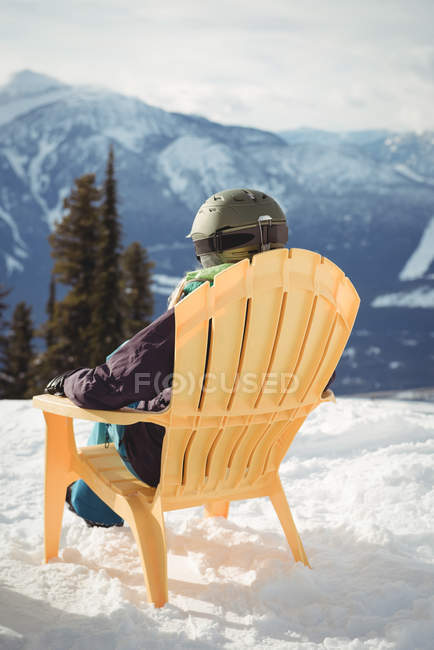 Visão traseira da mulher sentada na cadeira na montanha coberta de neve contra o céu — Fotografia de Stock
