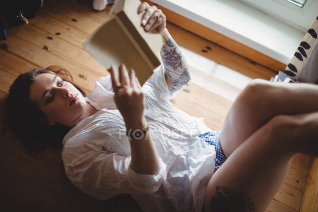 Frau liegt auf dem Boden und liest zu Hause ein Buch — Stockfoto