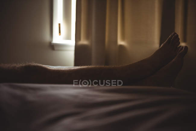 Мужчина отдыхает на кровати со скрещенными ногами в спальне дома — стоковое фото