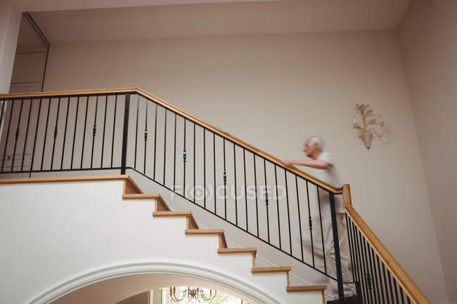 Старший мужчина поднимается по лестнице держа дома — стоковое фото