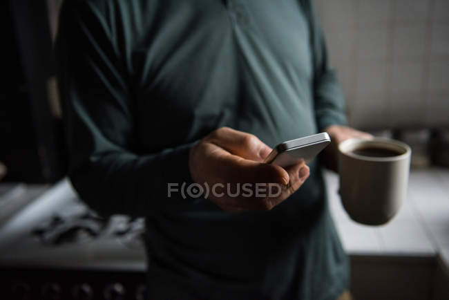 Середній розділ людини, що використовує мобільний телефон, маючи чашку кави вдома — стокове фото