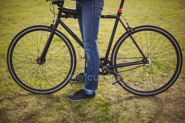 Нижняя часть женщины, стоящей с велосипедом на зеленой траве — стоковое фото