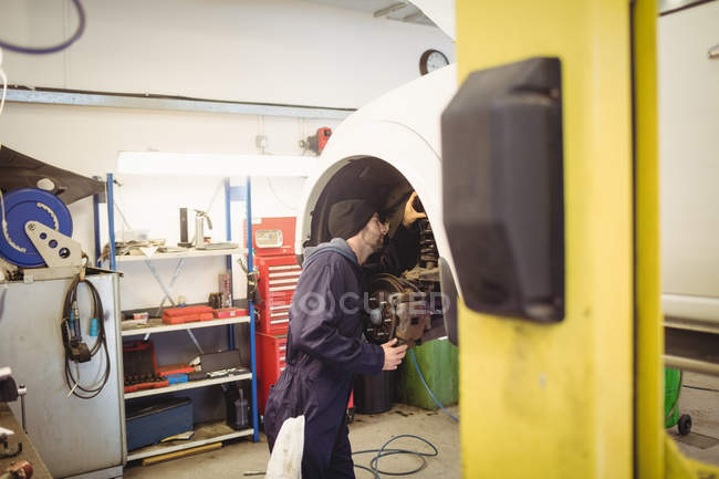 Mecánico examinando un freno de disco de la rueda del coche en garaje de reparación - foto de stock