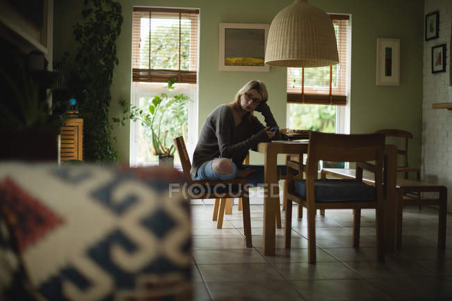 Жінка використовує мобільний телефон, сидячи вдома — стокове фото