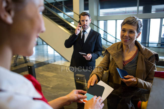 Female staff giving boarding pass to the passengers at the airport terminal — Stock Photo