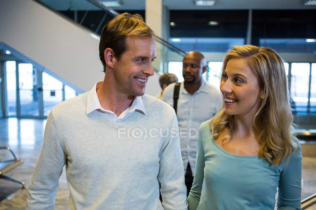 Усміхнена пара дивиться один на одного, стоячи в зоні очікування в терміналі аеропорту — стокове фото