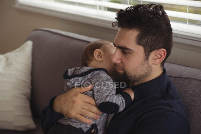 Padre che tiene il bambino seduto sul divano di casa — Foto stock