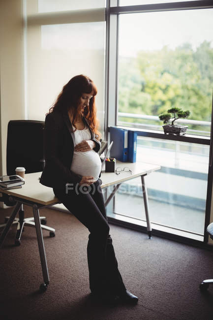 Embarazada mujer de negocios tocando vientre en la oficina - foto de stock