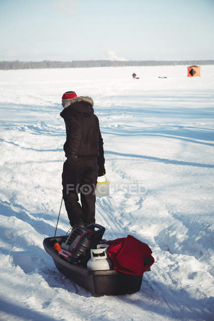 Pescatore di ghiaccio che trasporta attrezzi da pesca sul ghiaccio in un paesaggio innevato — Foto stock