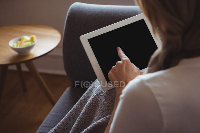Mulher usando tablet digital no sofá na sala de estar — Fotografia de Stock