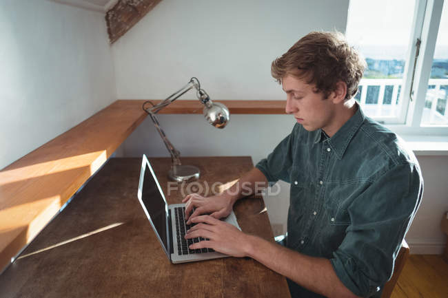 Uomo seduto alla scrivania e utilizzando il computer portatile in studio — Foto stock