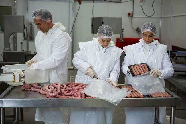 Carniceros empacando salchichas en el interior de la fábrica de carne - foto de stock