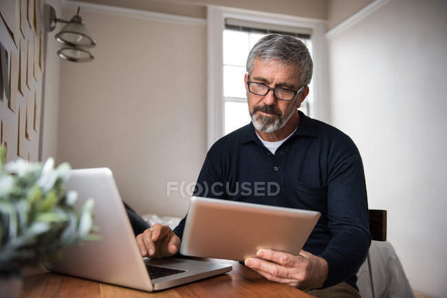 Uomo che utilizza laptop e tablet digitale in soggiorno a casa — Foto stock
