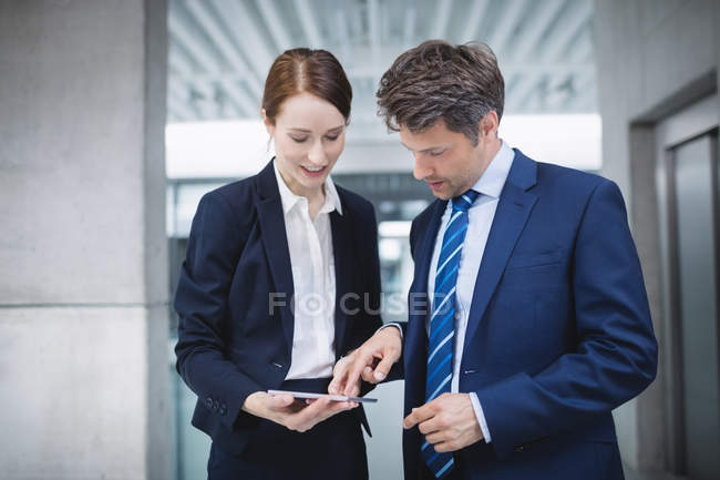 Empresario y colega discutiendo sobre tableta digital dentro del edificio de oficinas - foto de stock