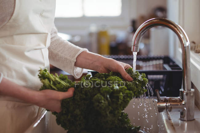 Sección media de la mujer que lava el brócoli debajo del fregadero en la cocina en casa - foto de stock