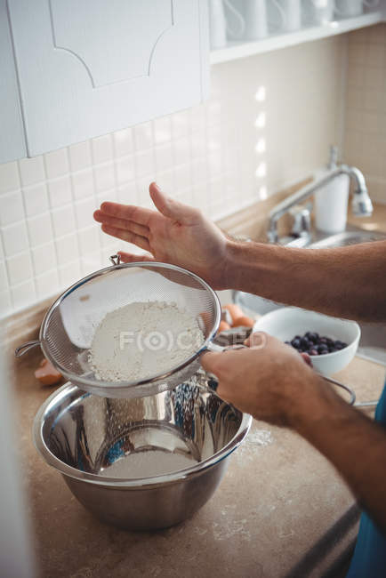 Man sifting flour into a mixing bowl in the kitchen at home — Stock Photo