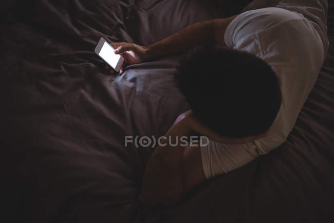 Человек, использующий свой мобильный телефон во время отдыха на кровати дома — стоковое фото