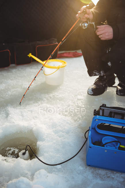 Mid section of ice fisherman sitting on chair in tent with fishing rod — Stock Photo