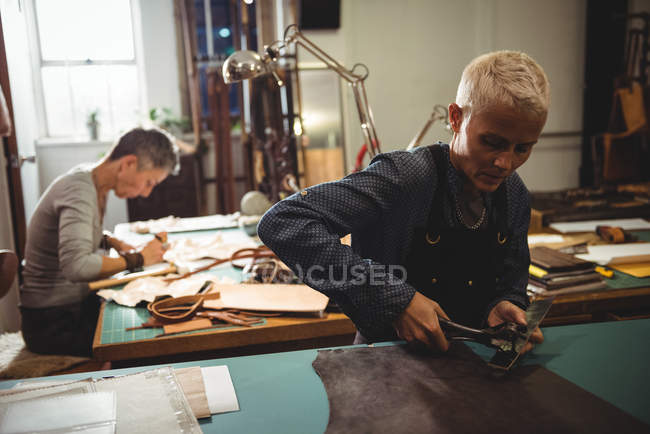 Craftswoman punching hole from leather punch machine in workshop — Stock Photo