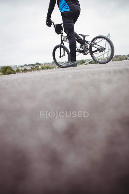 Ciclista de pie con bicicleta BMX en la rampa de salida en skatepark - foto de stock