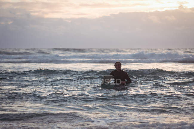 Portrait of a man carrying surfboard coming out of sea at dusk — Stock Photo