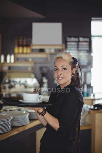 Retrato de garçonete de pé com xícara de café no café — Fotografia de Stock