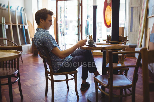 Seitenansicht eines Mannes, der mit dem Handy im Surfbrett-Geschäft sitzt — Stockfoto