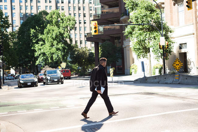 Empresário com um tablet digital atravessando a rua à luz do dia — Fotografia de Stock