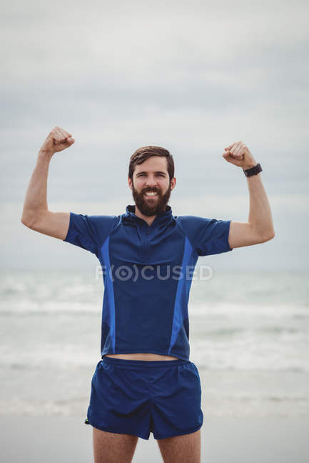 Portrait of athlete standing on beach with hands raised — Stock Photo