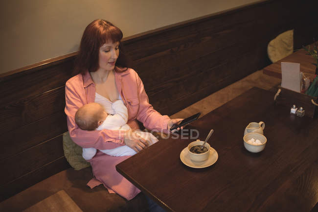 Mother with baby using mobile phone in cafe at table — Stock Photo
