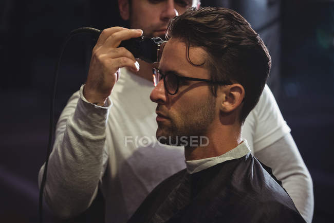 Man getting hair trimmed by stylist with trimmer in barber shop — Stock Photo