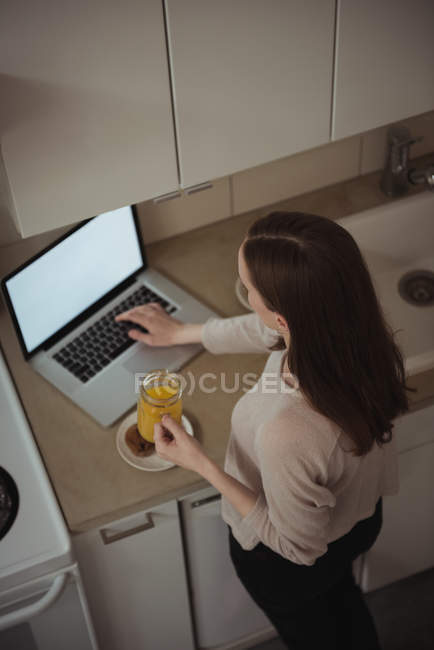 Женщина с ноутбуком во время завтрака на кухне дома — стоковое фото