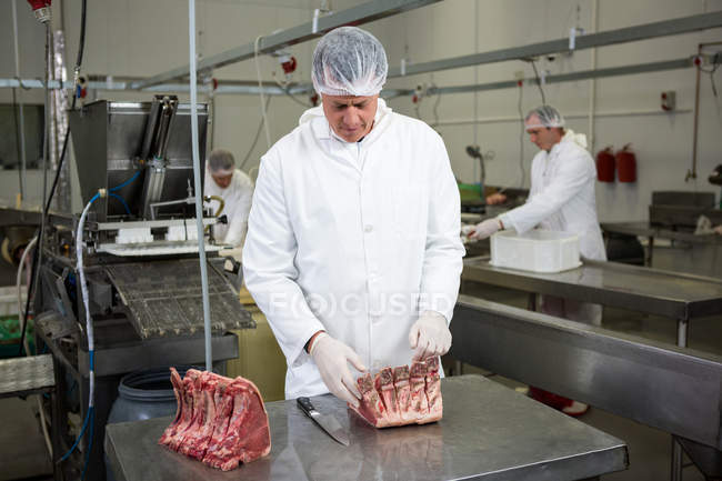 Carniceros cortando carne cruda en una máquina de sierra de cinta en la fábrica de carne - foto de stock