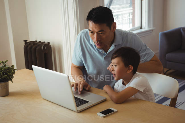 Батько і син використовують мобільний телефон і ноутбук у вітальні вдома — стокове фото