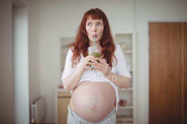 Femme enceinte réfléchie buvant du jus à la maison — Photo de stock